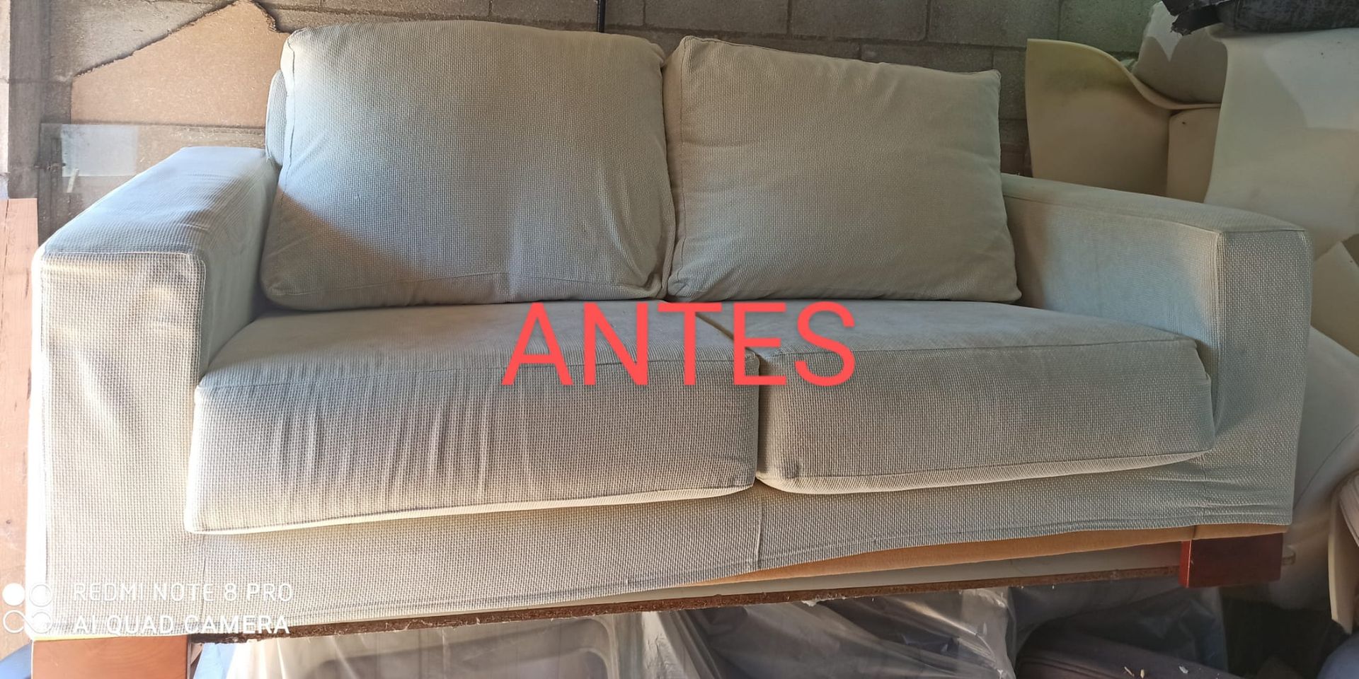Sofá blanco con cojines en una habitación, con la etiqueta “ANTES” en texto rojo.
