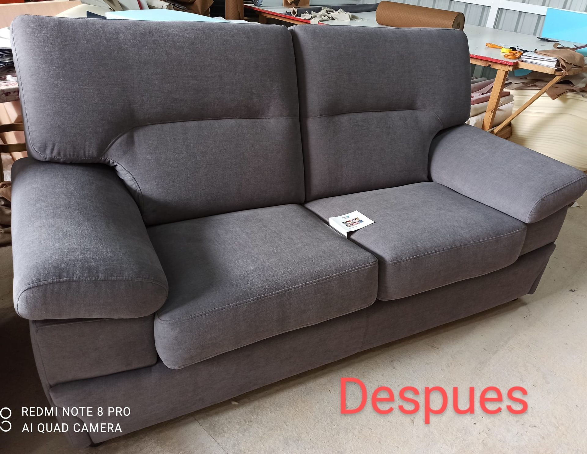 Sofá gris de 3 plazas en una habitación, con una etiqueta blanca en el cojín y el texto 