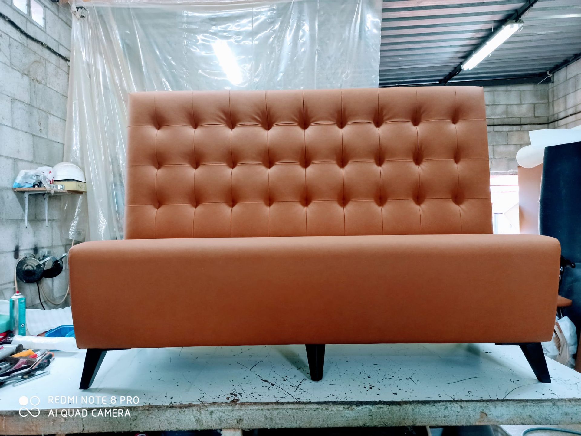 Sofá capitoné naranja en un taller, con respaldo alto capitoné y patas negras.