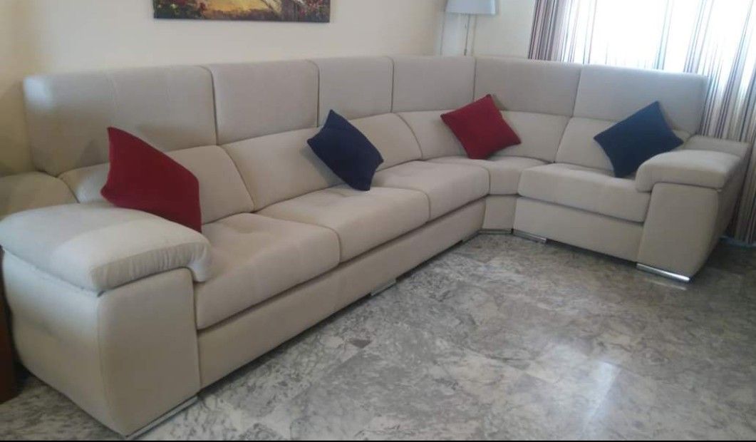 Sofá seccional beige en forma de L con cojines rojos y azules sobre un suelo de mármol.
