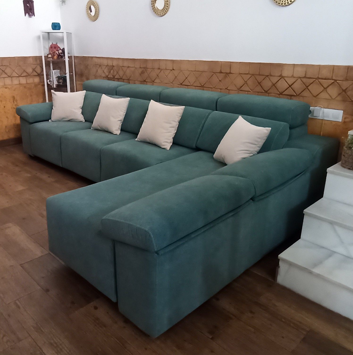 Sofá modular verde con cojines beige en una sala de estar junto a una escalera.