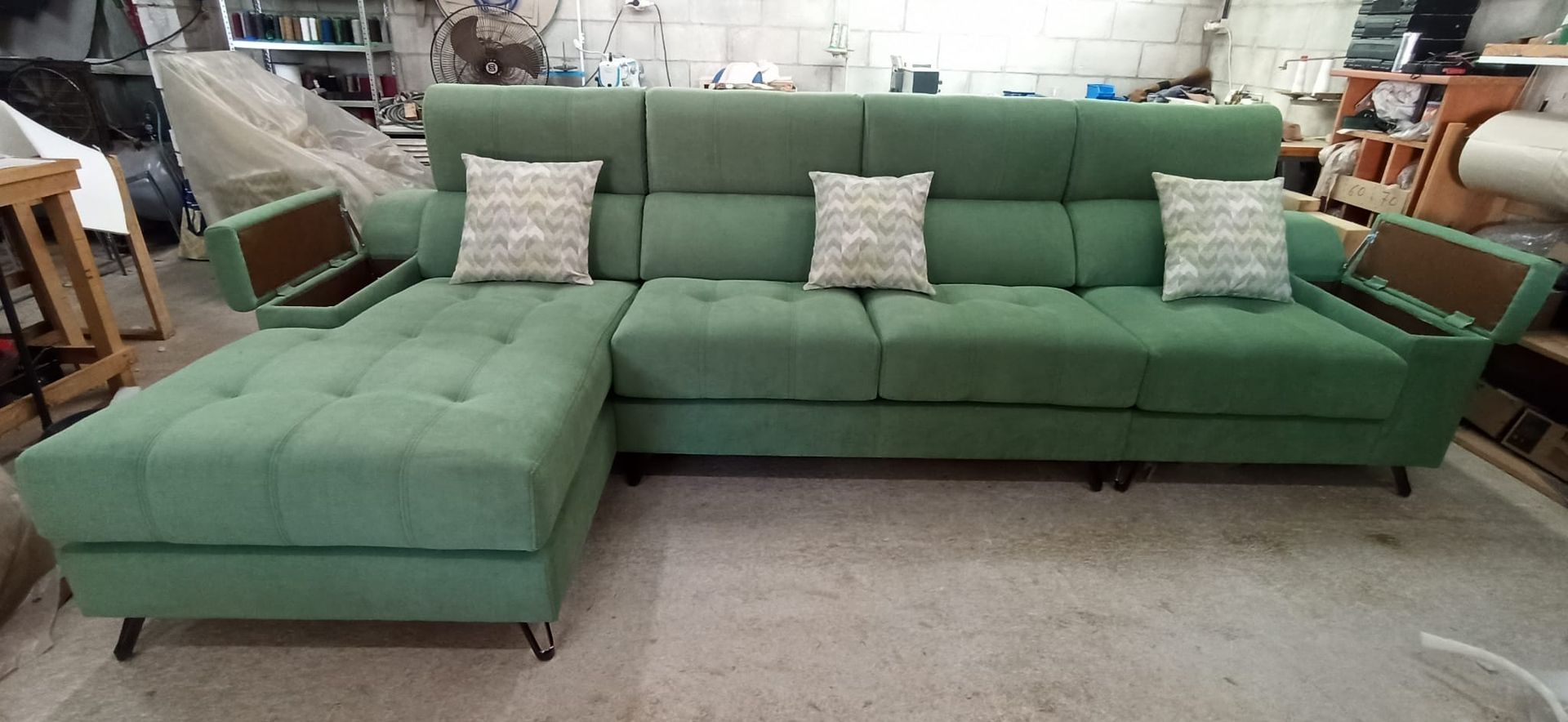 Sofá modular verde con chaise longue y tres cojines decorativos estampados en una exposición de muebles.