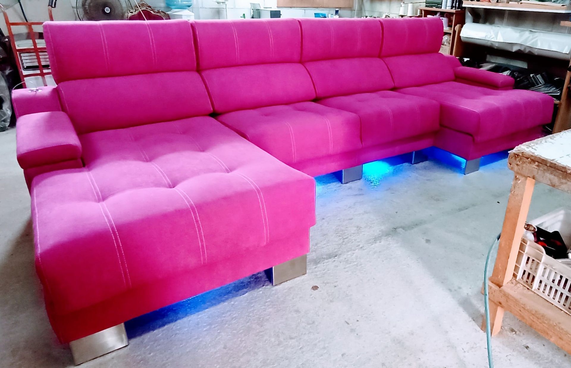 Sofá modular de color rosa brillante en una sala de estar, iluminado por luces LED azules desde abajo.