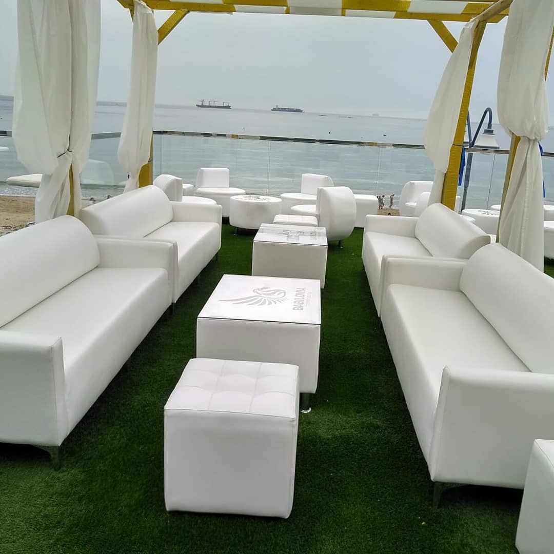 Sofás blancos bajo un toldo en una terraza cubierta de césped junto al mar.