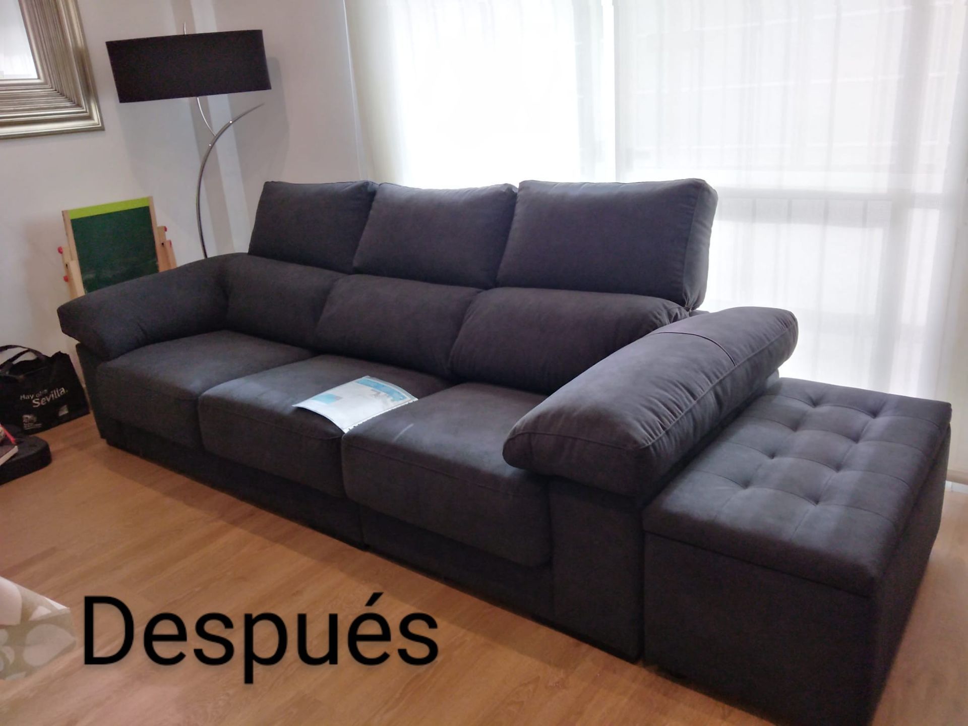 Sala de estar con sofá gris oscuro y chaise longue, junto a ventana con cortinas blancas.