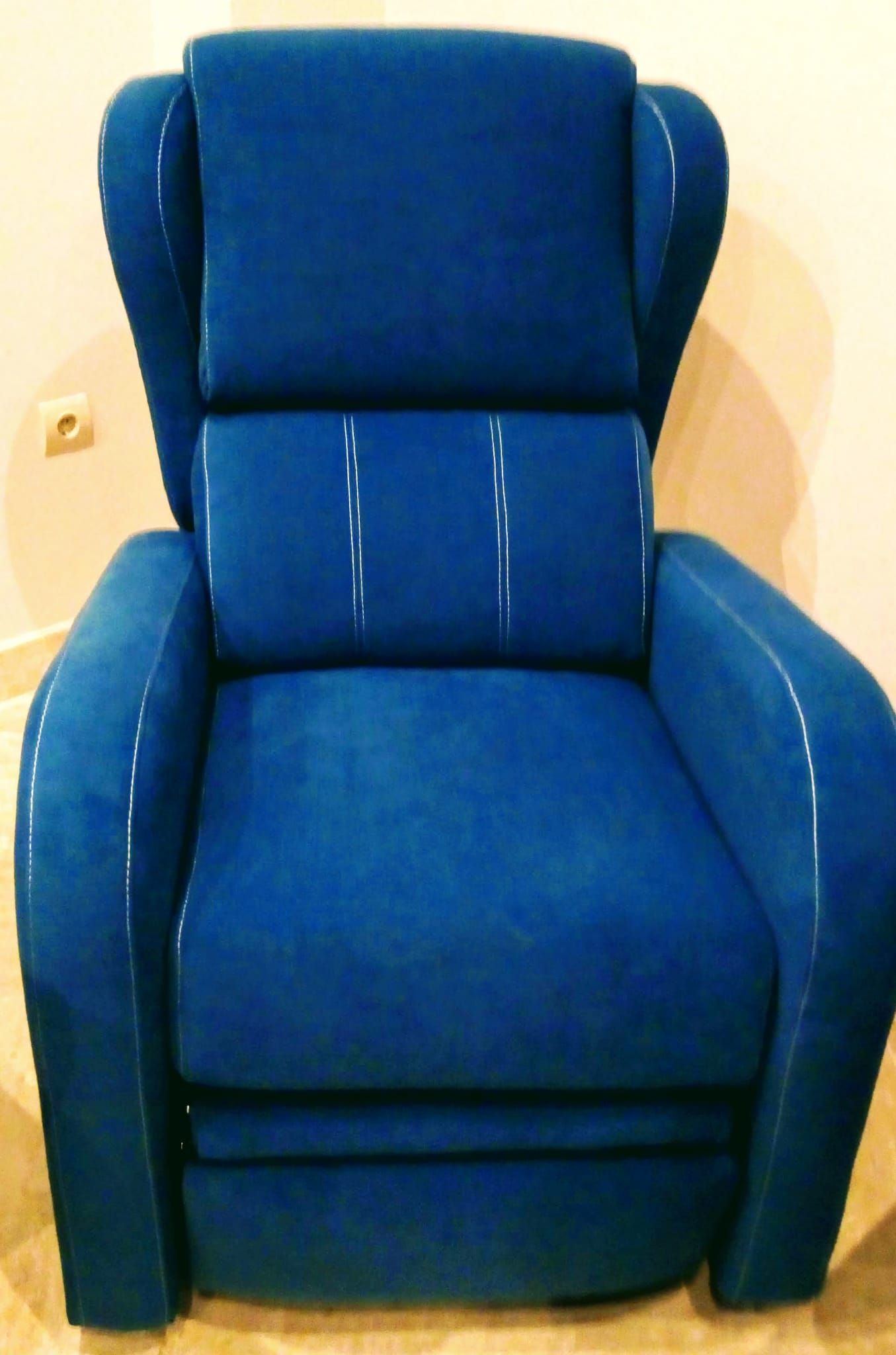 Sillón tapizado en azul contra una pared beige.