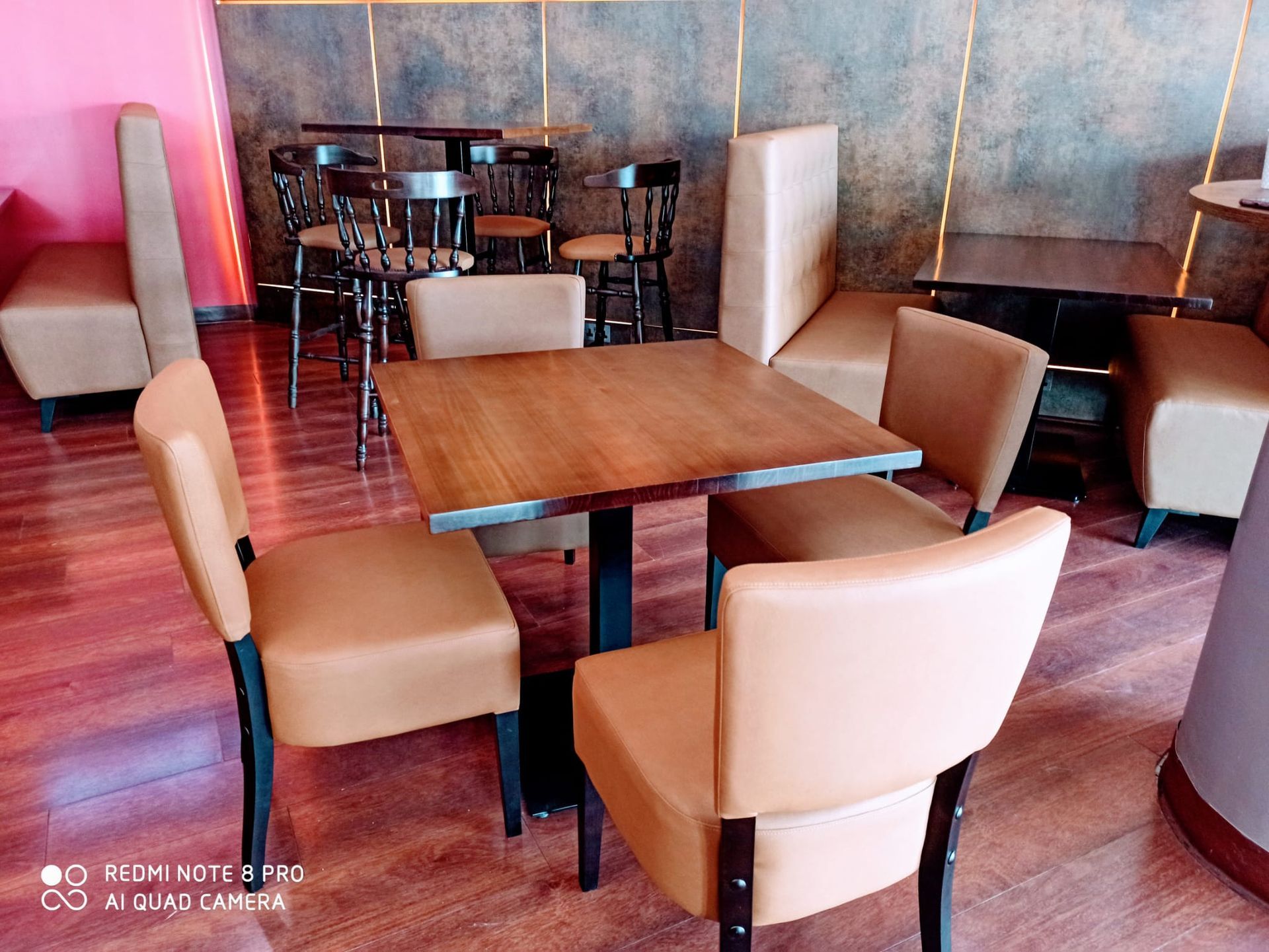 Zona de estar vacía de una cafetería con sillas color canela y mesas de madera sobre un suelo de baldosas rojas.