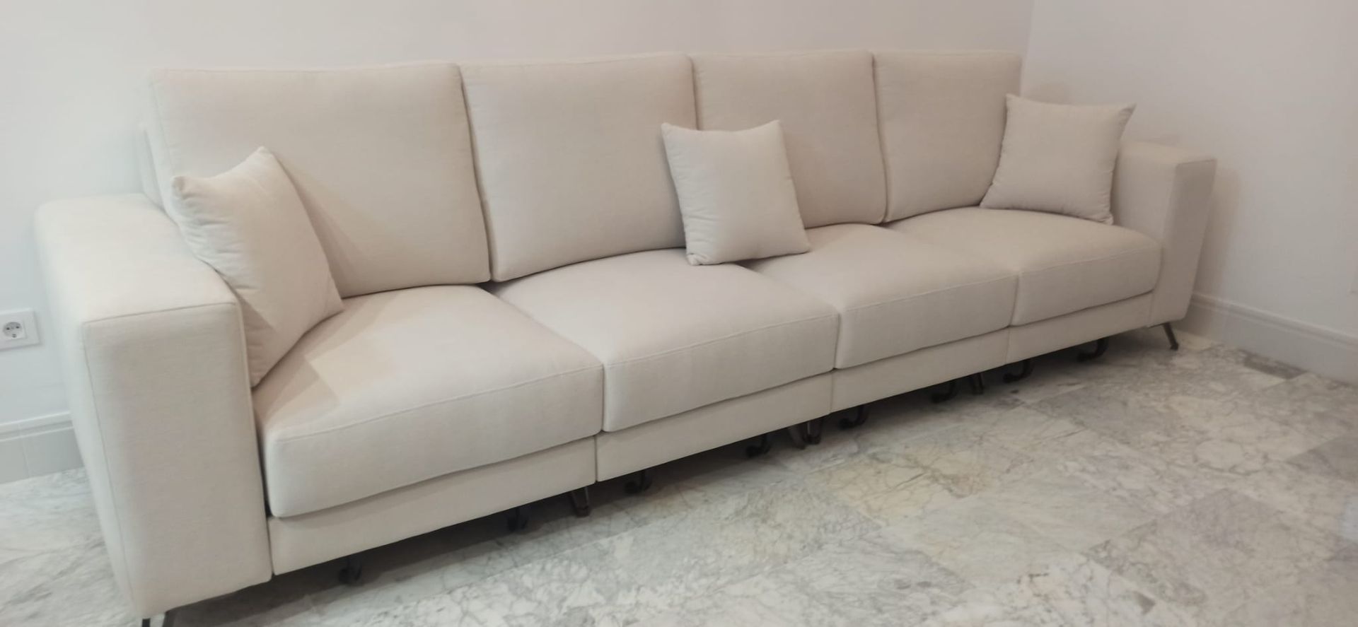 Sofá seccional beige con cojines contra una pared blanca sobre una alfombra clara.