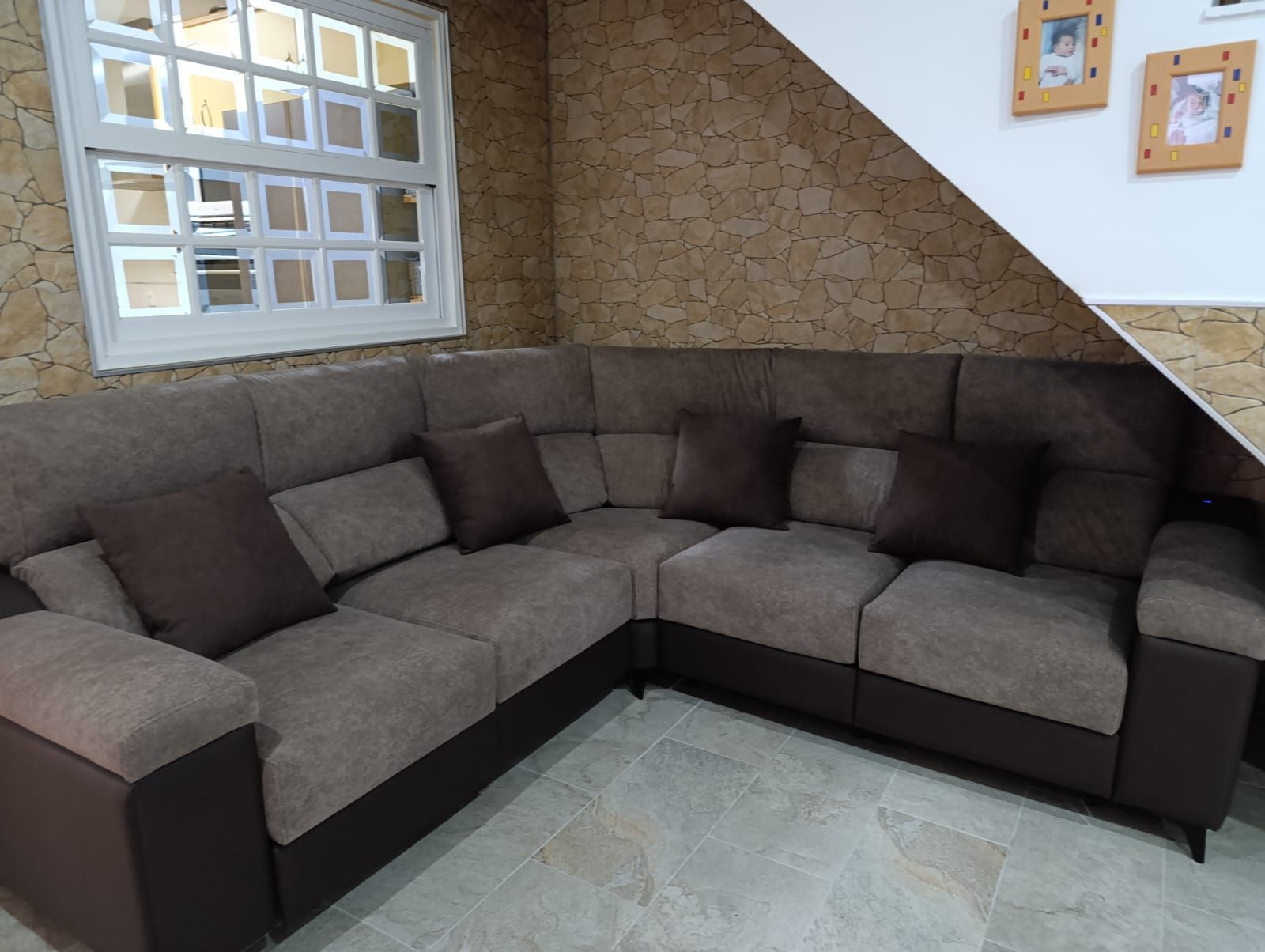 Sofá seccional gris en forma de L en un salón de esquina con paredes color canela y una ventana de bloques de vidrio.