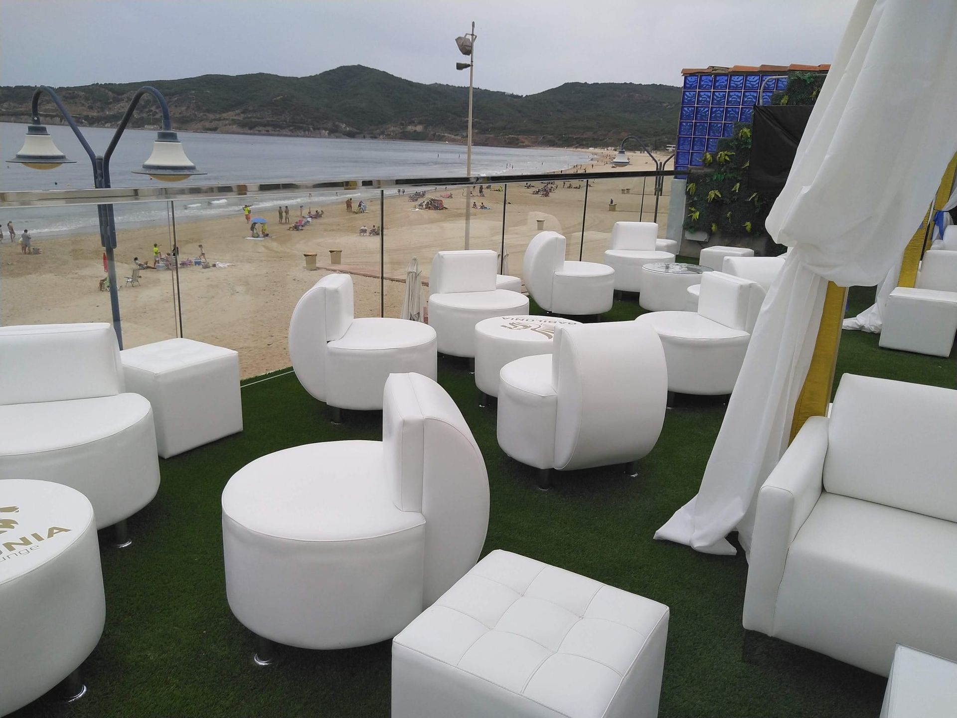 Sofás blancos en una terraza junto a la playa con vistas al océano, con una mesa y un toldo.