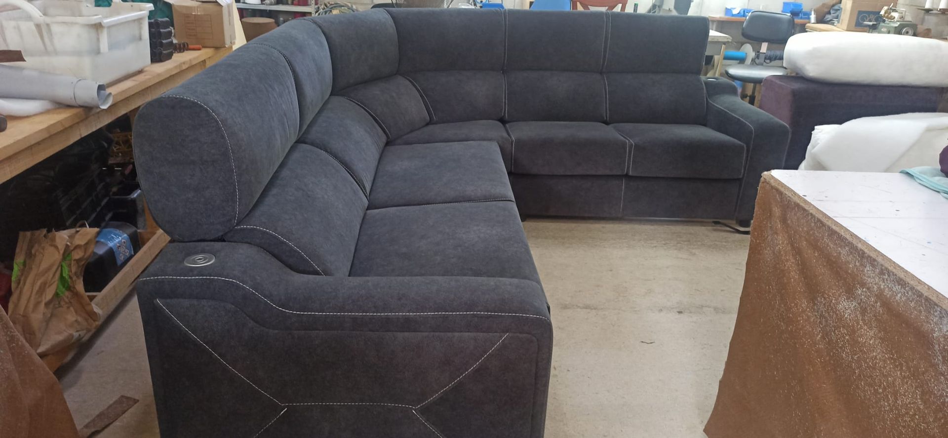 Sofá seccional gris oscuro en la sala de exposición de una tienda de muebles, con cajas y otros muebles cerca.