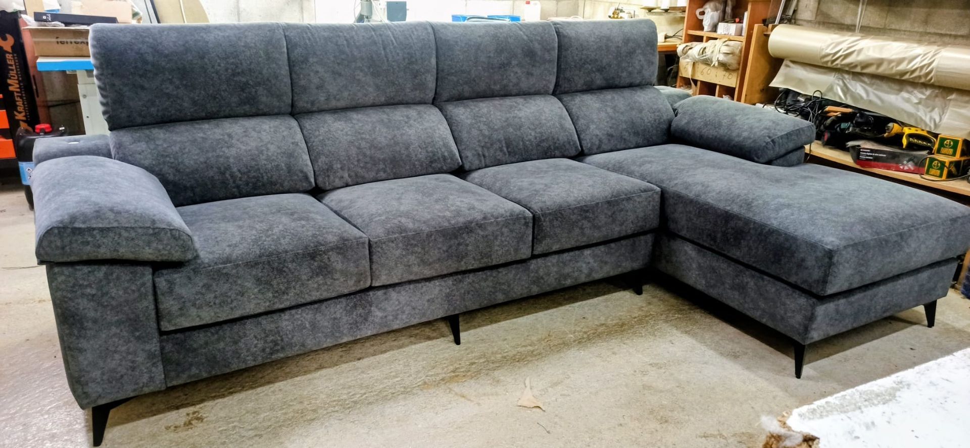 Sofá seccional tapizado en color gris en un taller o sala de exposición, con una chaise longue a la derecha