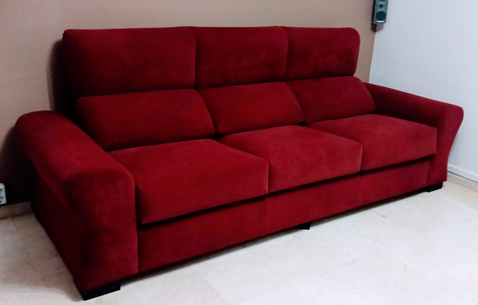 Sofá tapizado en rojo en una habitación de color claro, con una pared blanca de fondo.