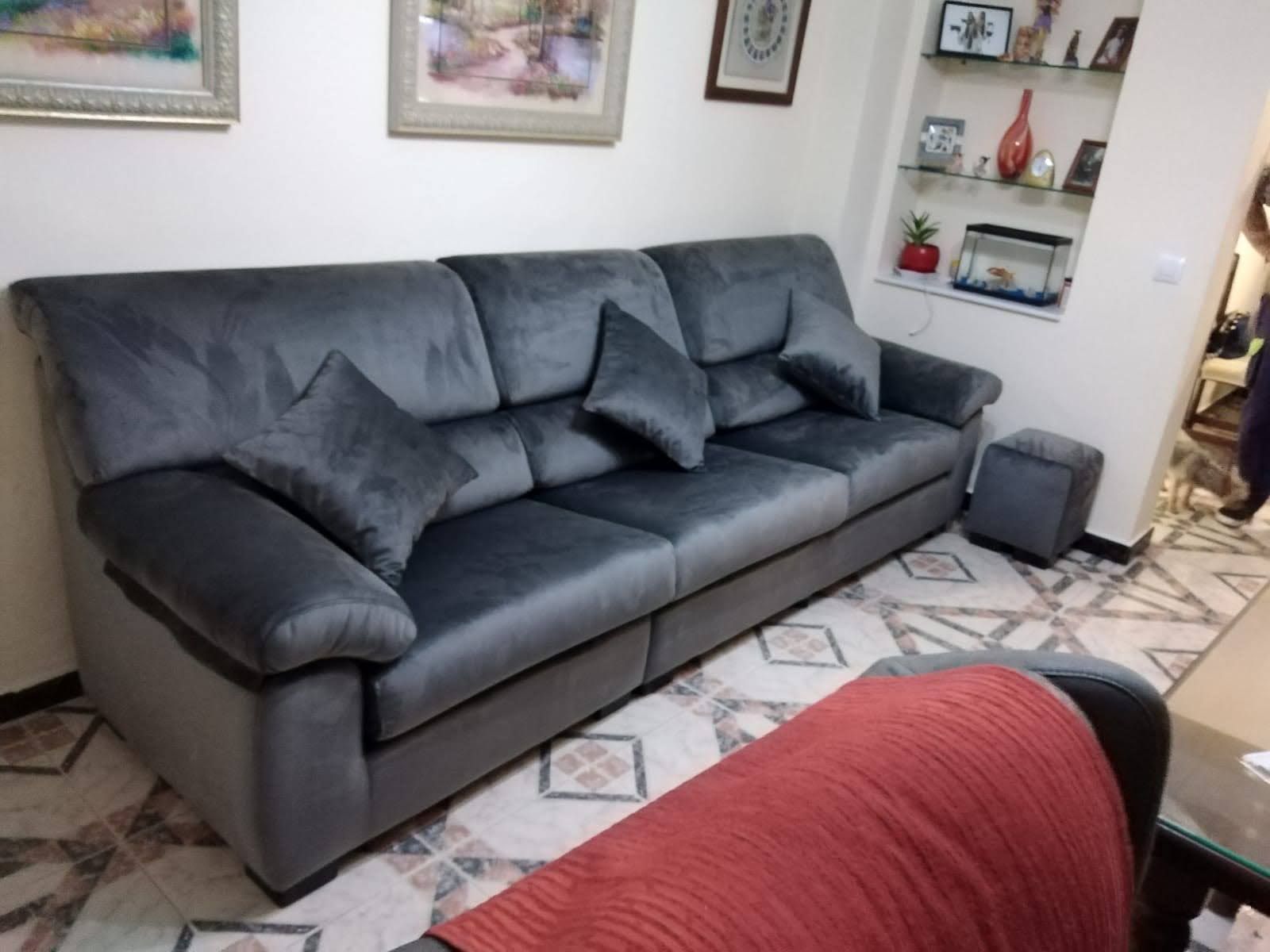 Sofá modular gris con cojines oscuros en una sala de estar con cuadros enmarcados y una alfombra estampada.