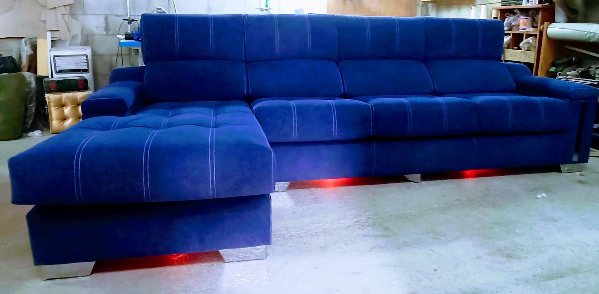 Sofá modular azul en una habitación, con luces rojas brillando debajo.