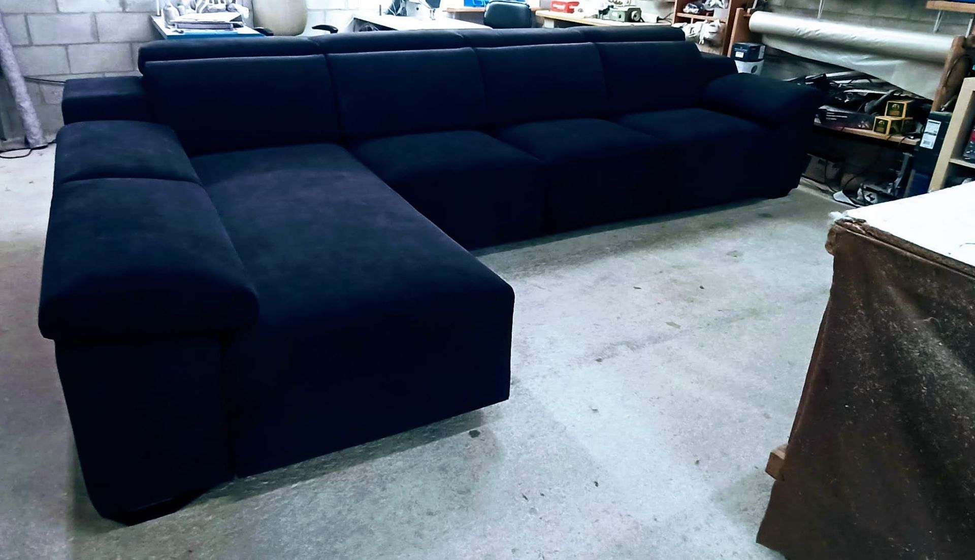 Sofá seccional azul marino oscuro en una sala de exposición o taller sobre un suelo de hormigón.