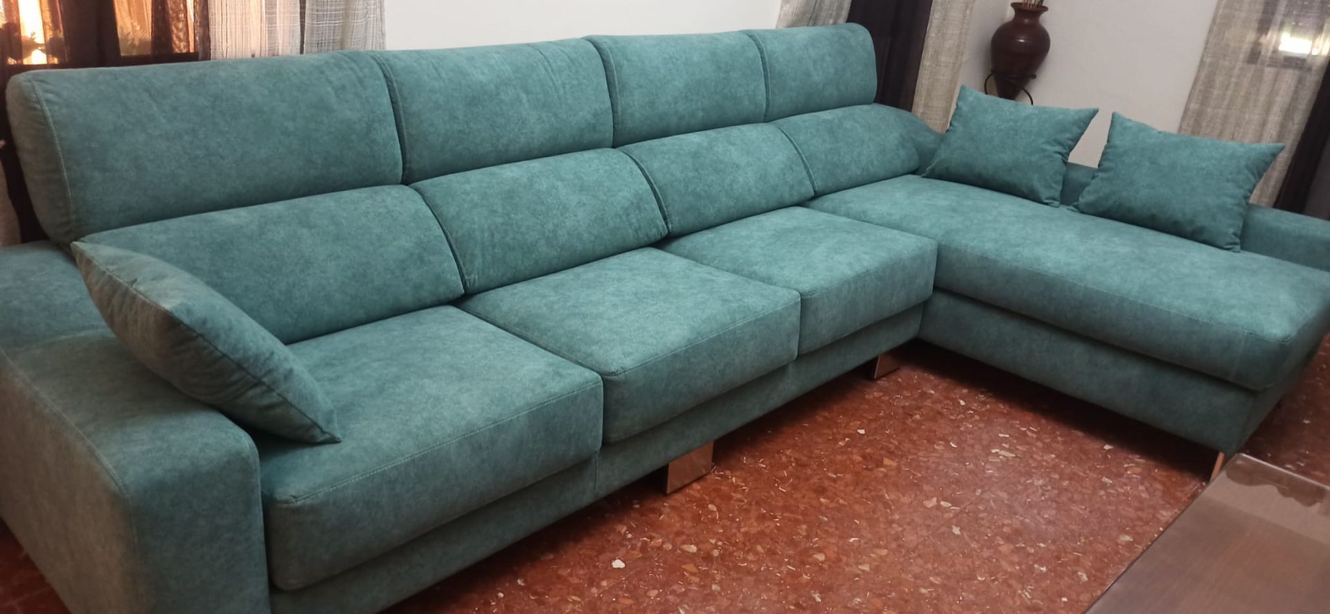 Sofá seccional color turquesa con chaise longue en una sala de estar sobre un suelo de baldosas rojizas.