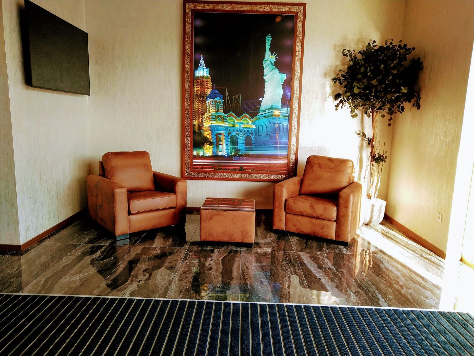 Elegante salón con dos sillones color canela, una mesita, suelo de mármol y un cuadro iluminado