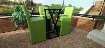 Dos sillas verde lima y una mesa negra en un patio de grava con una planta en maceta y vistas al jardín.