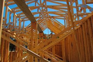Se está construyendo una casa con vigas de madera y un cielo azul al fondo.
