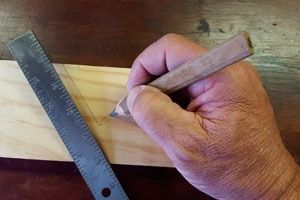 Una persona está midiendo un trozo de madera con una regla y un lápiz.