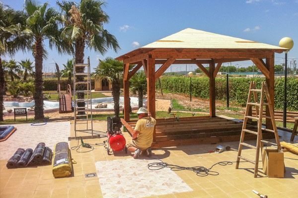 Un hombre está trabajando en un cenador de madera al lado de una piscina.