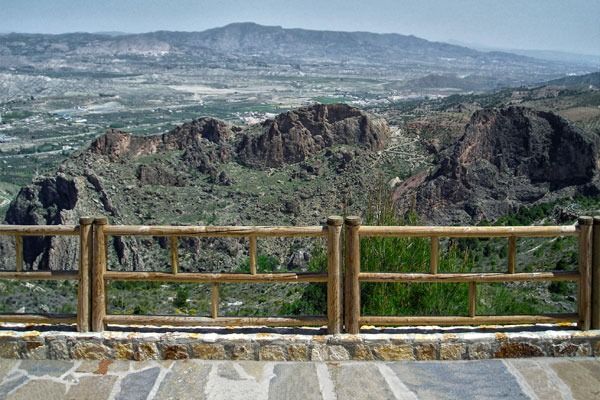Una valla de madera con vistas a un valle con montañas al fondo.