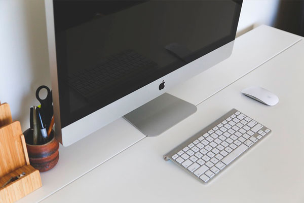 Una computadora Apple está sobre un escritorio blanco al lado de un teclado y un mouse.