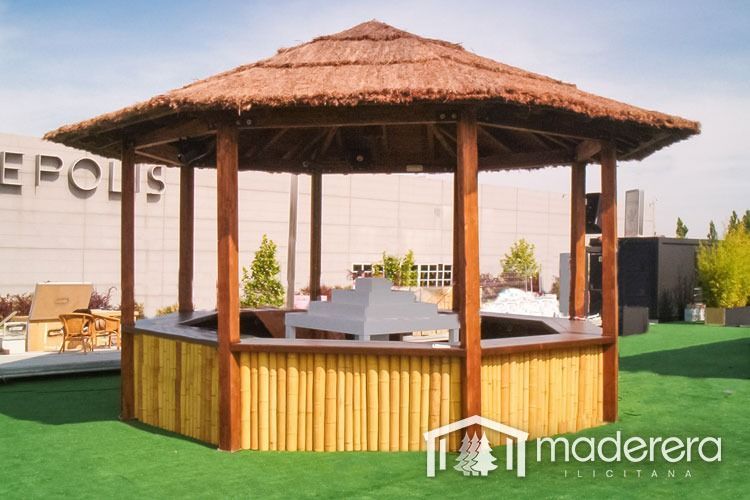 Un cenador de madera con techo de paja frente a un edificio que dice epols