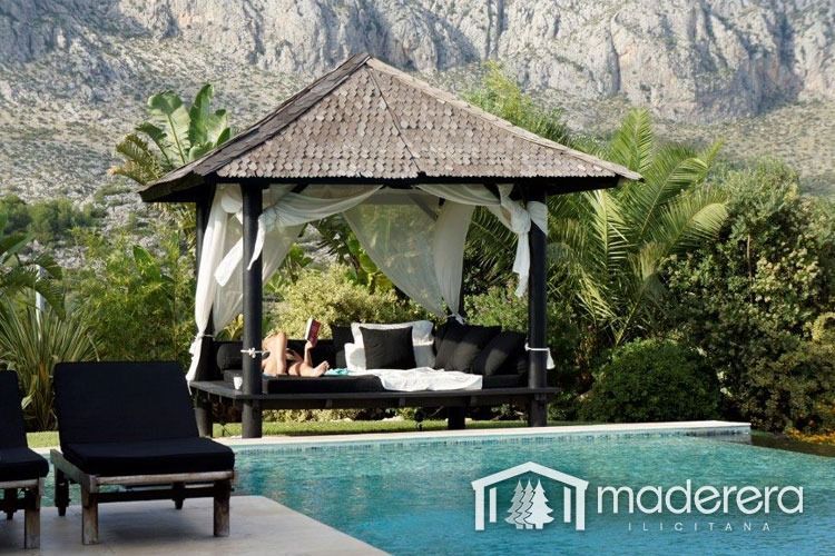 Una mujer se sienta bajo un cenador junto a una piscina.