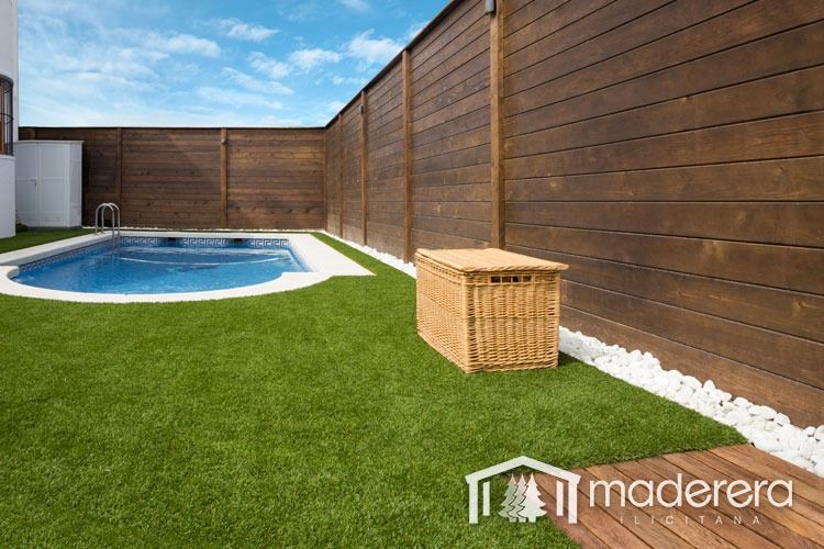 Una valla de madera rodea una piscina en un patio trasero.
