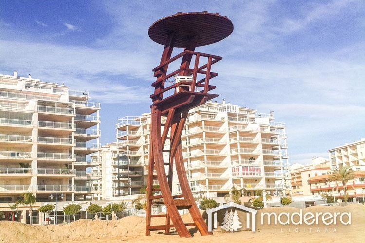 Una torre de salvavidas de madera en una playa con edificios al fondo.