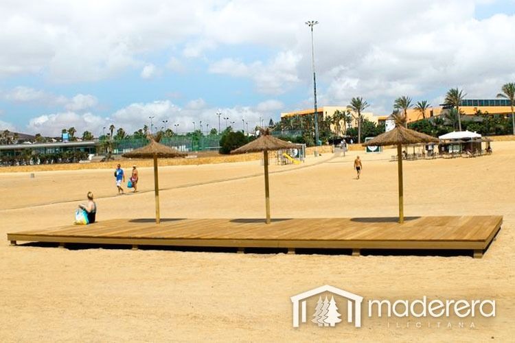 Una plataforma de madera con sombrillas en una playa de arena