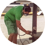 Un hombre que lleva una camisa verde y pantalones cortos verdes está trabajando en una pieza de metal.