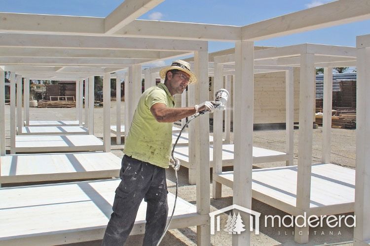 Un hombre está pintando con aerosol una estructura de madera con la palabra madera en la esquina.