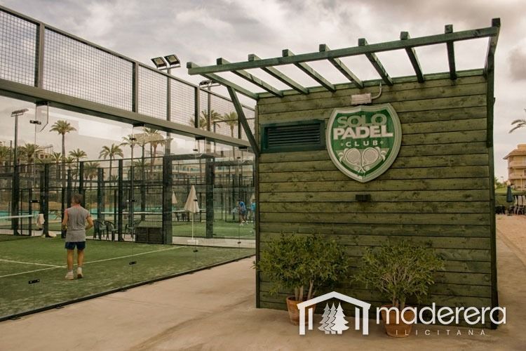 Un hombre está parado frente a un edificio de madera que dice Solo Padel.