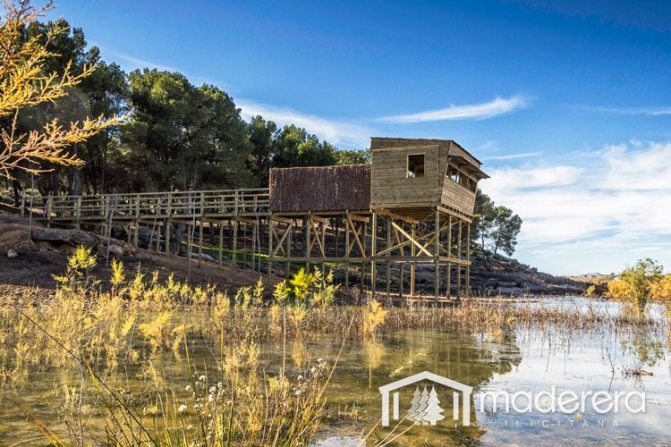 Un edificio de madera está situado encima de un lago rodeado de árboles.