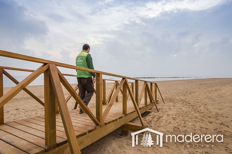 Un hombre está parado en un puente de madera sobre una playa de arena.