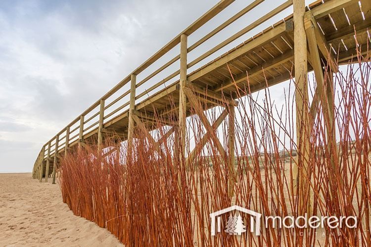 Un puente de madera sobre una playa de arena con una valla de madera en primer plano.