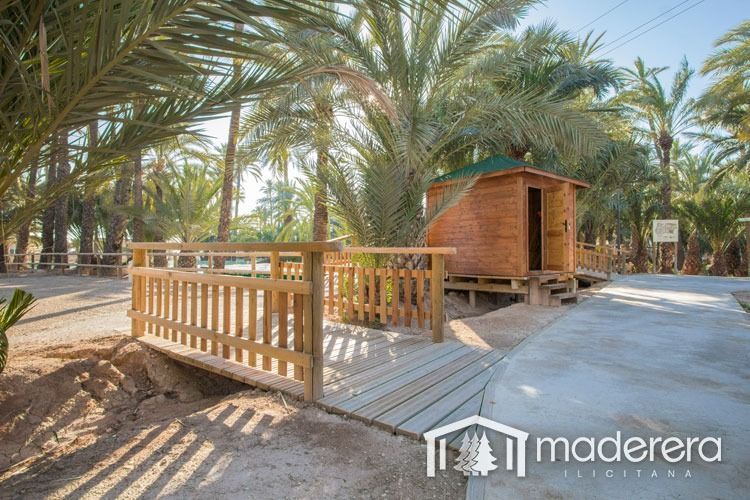 Una pequeña casa de madera está rodeada de palmeras y un puente de madera.