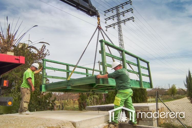 Dos hombres están levantando un puente verde con una grúa.