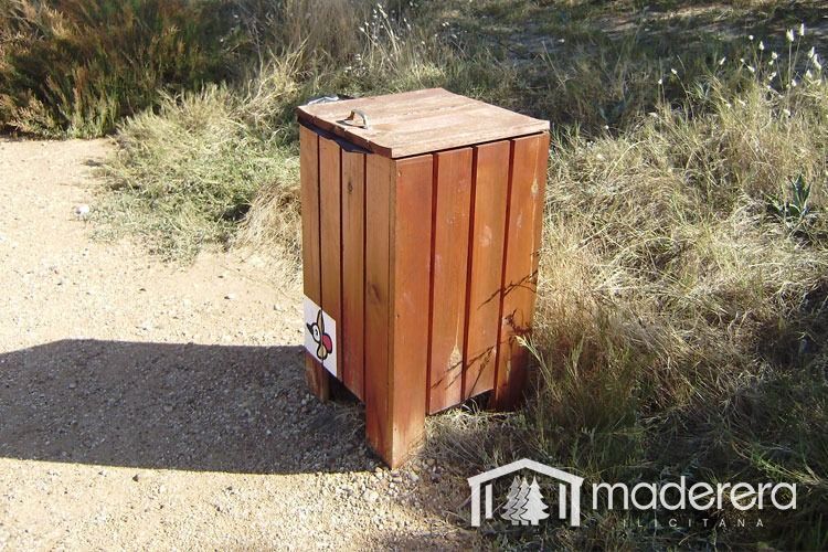 Un bote de basura de madera está tirado al costado de un camino de tierra.