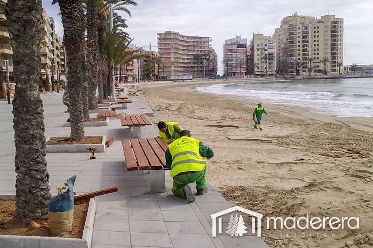 Un grupo de personas está trabajando en una mesa de picnic de madera en una playa.