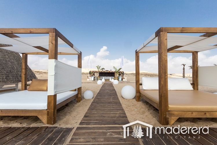 Una pasarela de madera entre dos camas con dosel en una playa.