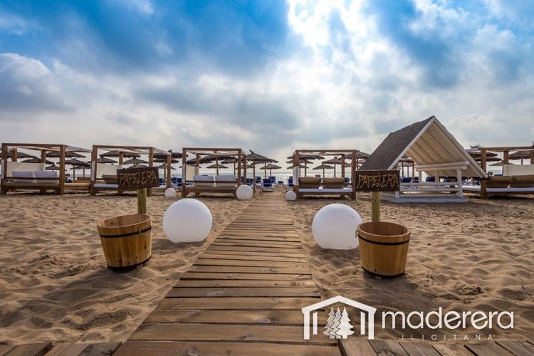 Una pasarela de madera que conduce a una playa con tumbonas y sombrillas.