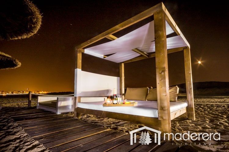 Una cama con dosel de madera está en la playa por la noche.