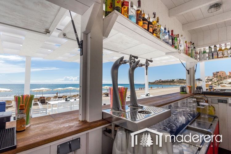 Un bar con vista al mar y botellas de alcohol en el estante.