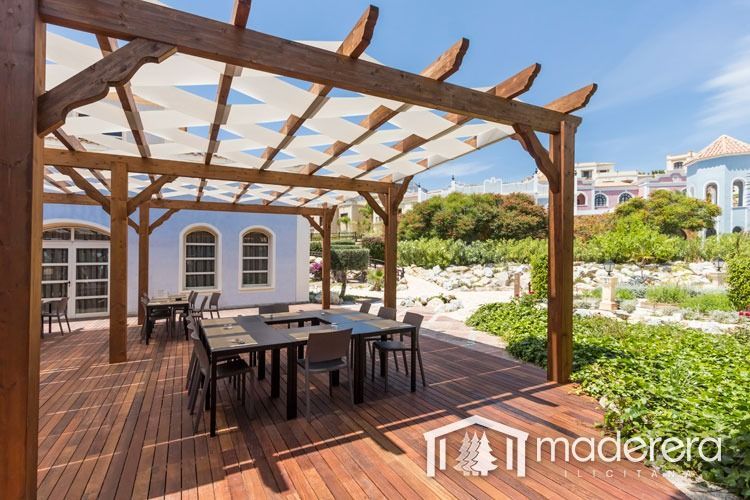 Una pérgola de madera con mesas y sillas debajo.
