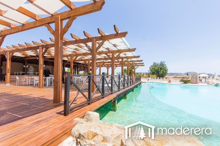 Una terraza de madera con pérgola con vistas a una piscina.