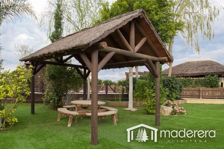 Un cenador de madera con techo de paja y una mesa de picnic debajo.